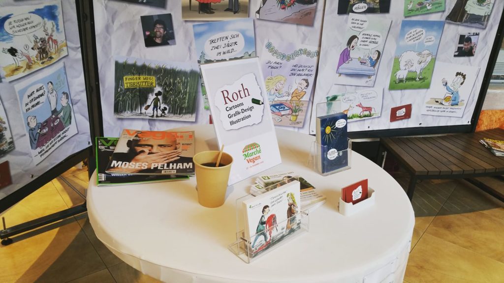 Stehtisch mit Postkarten und Visitenkarten von Cartoonist Stefan roth - roth-cartoons in Ulm im Blautalcenter beim marche vegan 2018